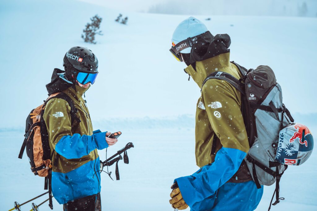 two skiers in north face kit do a transceiver test