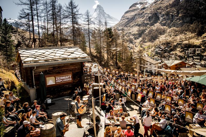 the snowy Matterhorn in the long distance, with a crowd of people celebrating at a mountain festival in the foreground