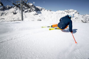 a skier carves deep by a chairlift line on a blue run