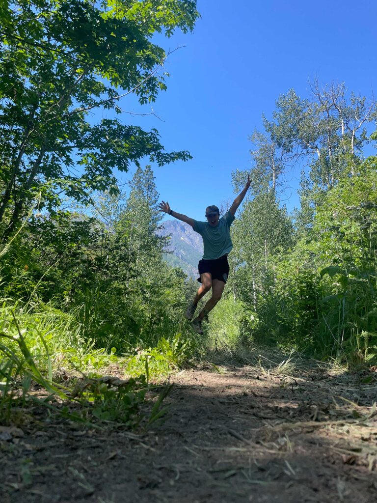 a summer shot from the trail with a woman running and jumping with arms in air, photo taken from ground