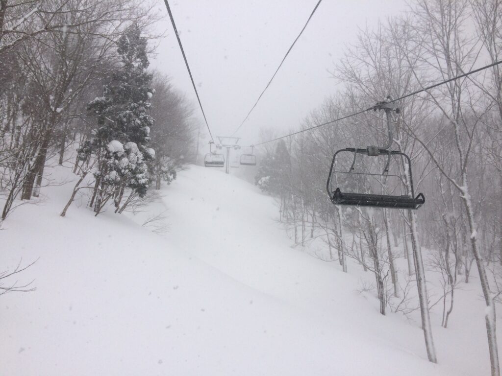 a quad chairlift is empty, pictured on a snowy day with a sweet looking line to ski underneath