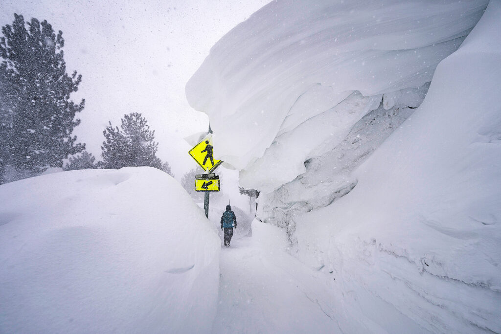 A person walks down a passage way loaded with snow, a huge metres-deep overhang of snow above him