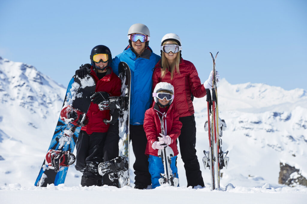 A family of four pose for a photo in the mountains, skis and snowboards in hand