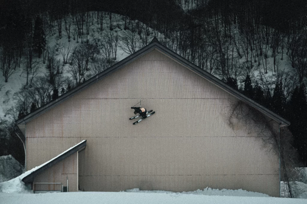 skier vertical on a huge barn's empty wall, having taken air off a lower roof