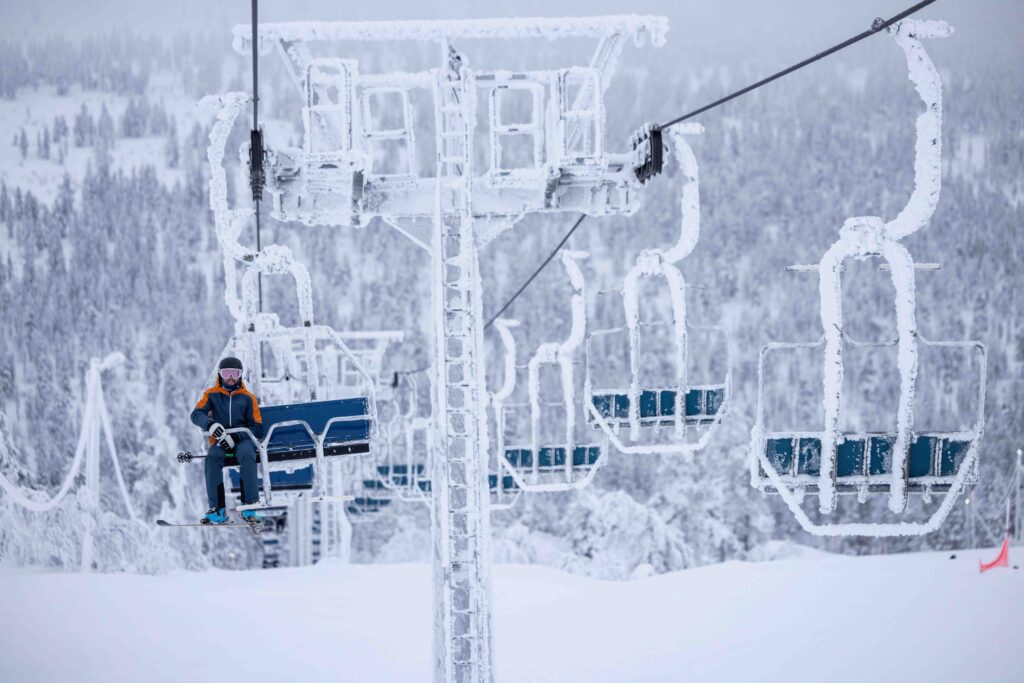 rime ice coats a chairlift, in a cold looking setting with a lone skier sat on said chairlift