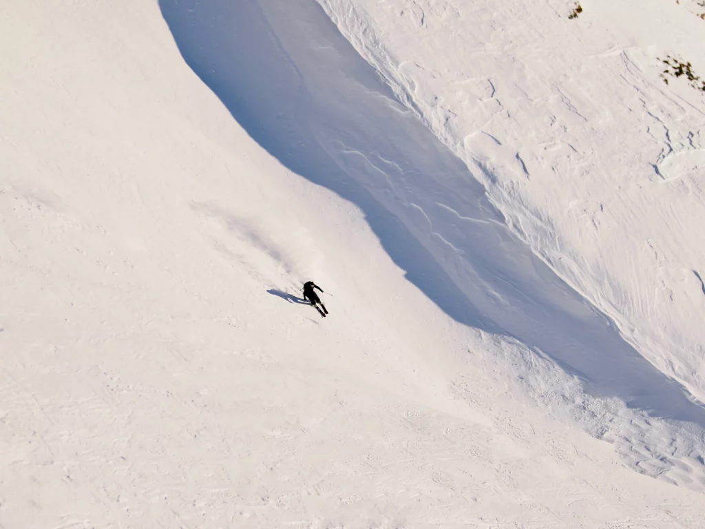 a skier makes turns next to the shadow line of a lip