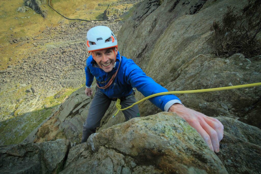Martin Chester smiles into camera half way up a rock |(climbing)
