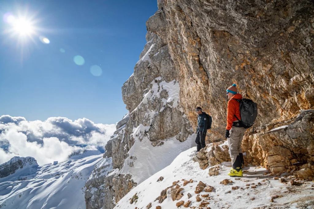 two skiers looking over cliff, high in snowy mountains