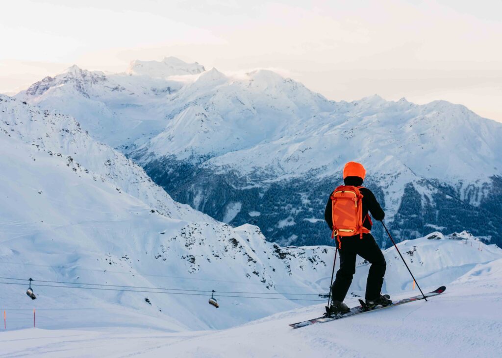 man in orange hat and pack looks out over a snowy Verbier ski area