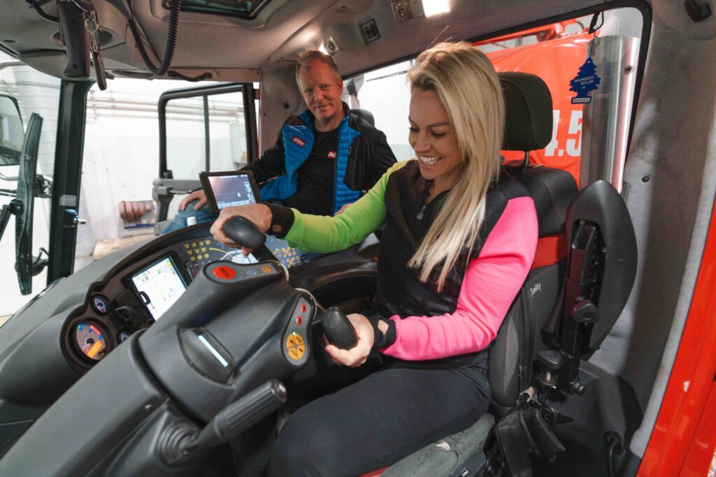 Ex ski racer Chemmy Alcott laughs as she sits inside a snow grooming machine cabin, with the driver, pretending to drive it