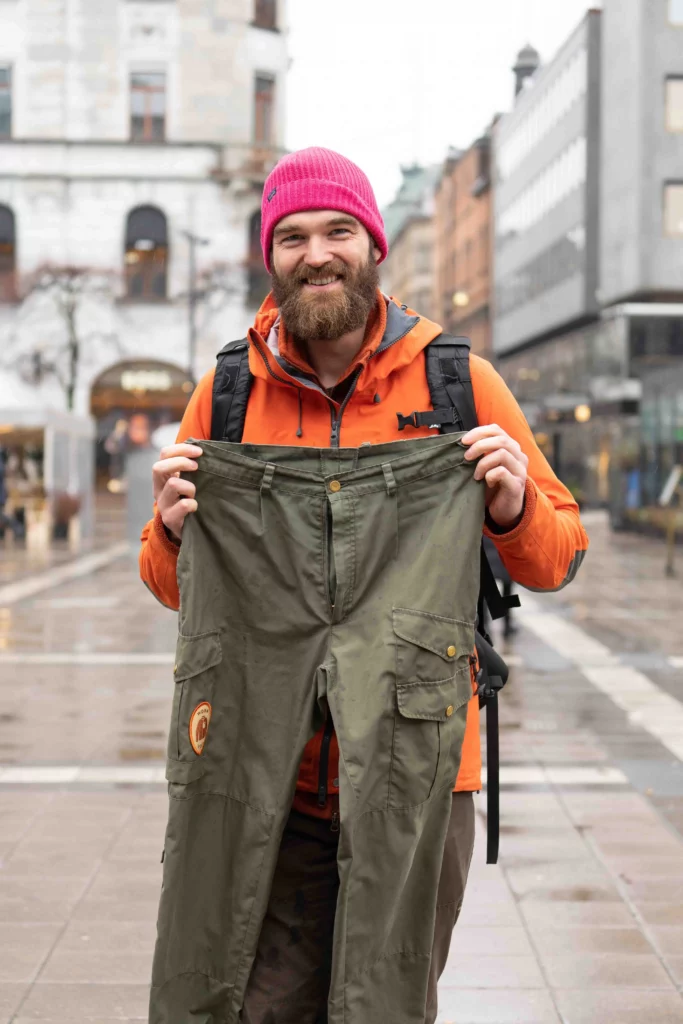 a man in the street holds up a pair of newly repaired green trousers
