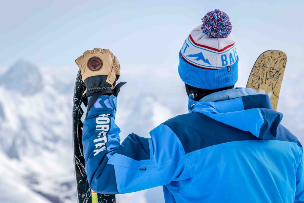 a skier holds tip of upright ski with gloved hand, next to his head, as he looks out over view - in a competition post to win Baïst