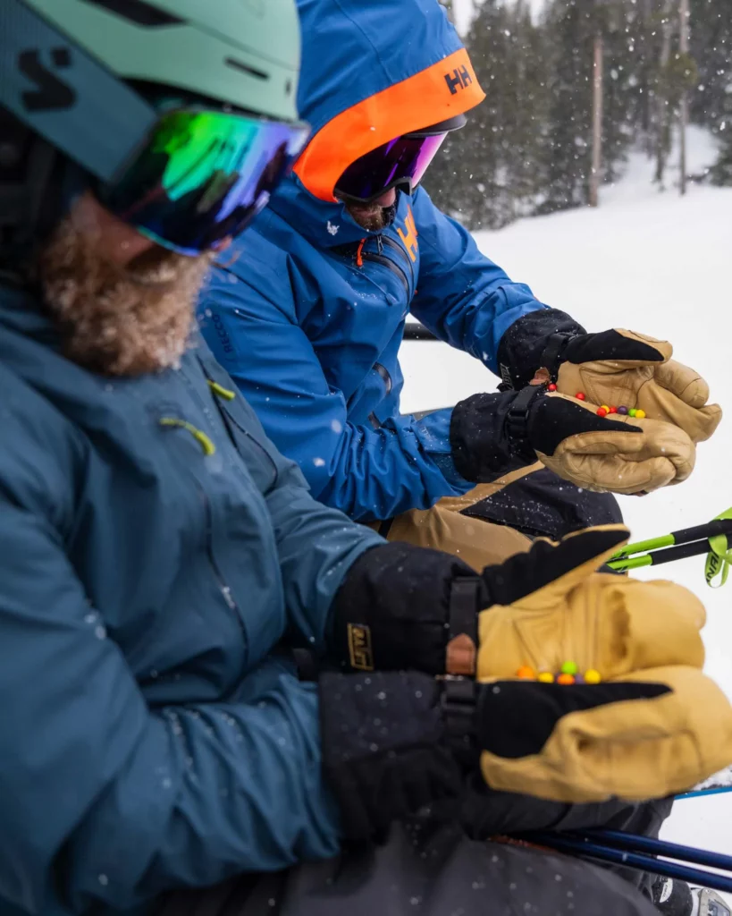 two skiers hold sweets in their mittens on a chairlift - in a competition post to win Baïst gloves