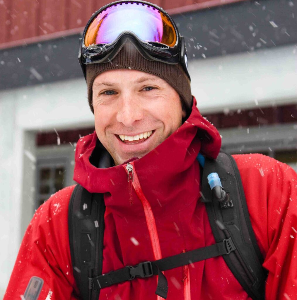Mark Brigham, marketing guru at Ellis Brigham, smiles into camera in a red ski jacket, out in the snow