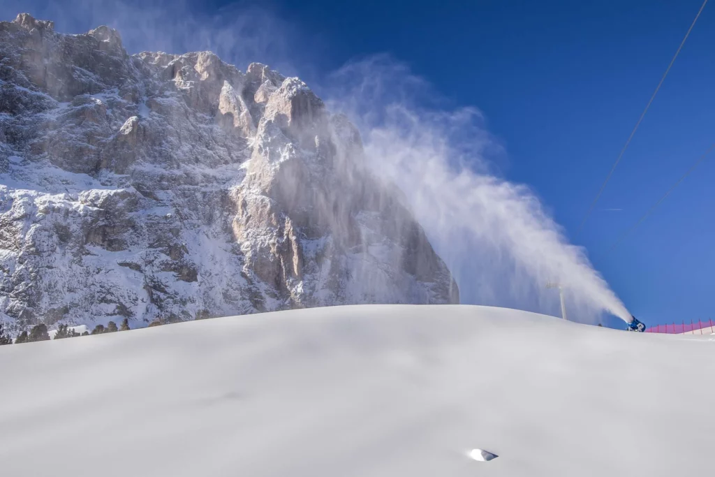 a snow cannon fires at the top of a mountain, against a blue sky