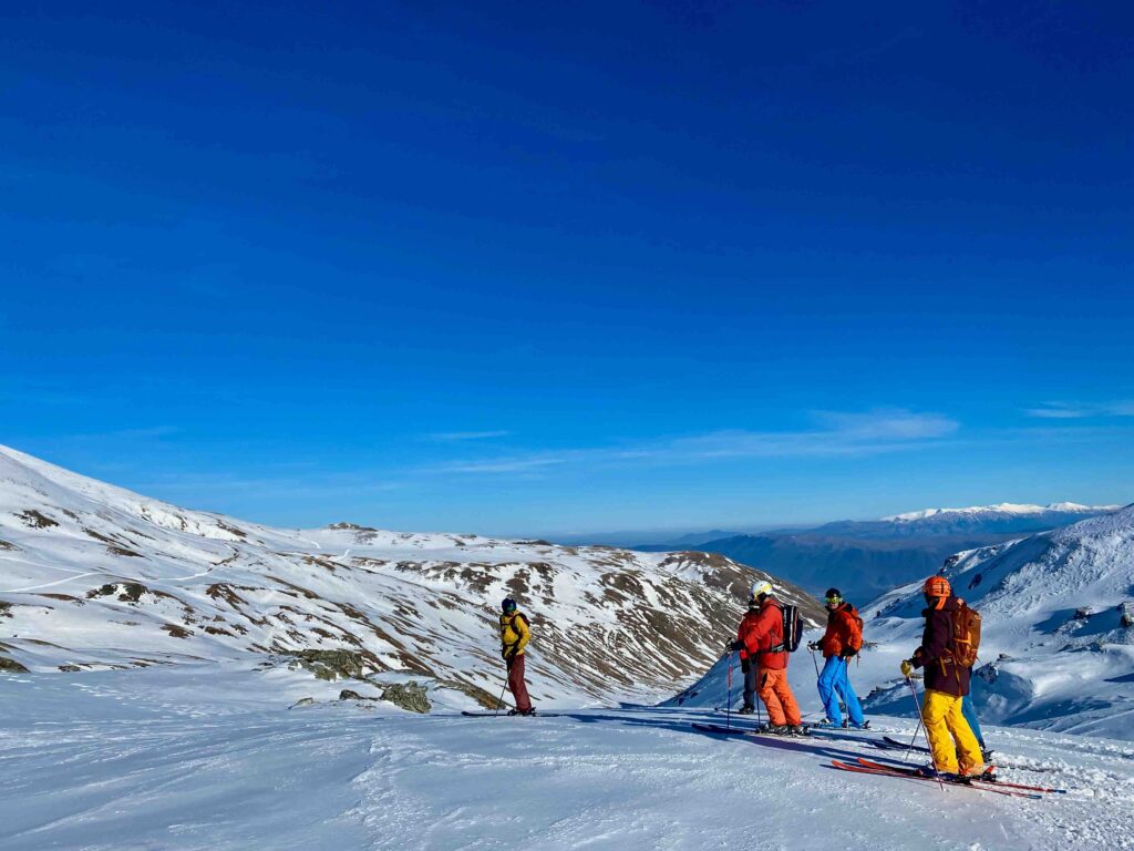 ski crew on a snowy hill in the backcountry, under blue skies