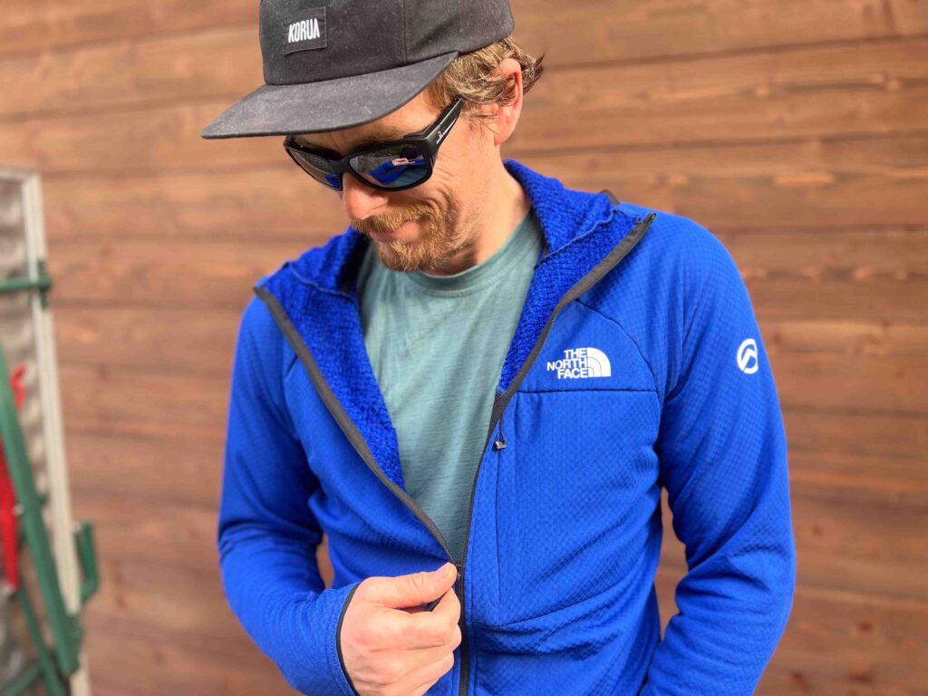 man models The North Face midlayer, in blue, by wooden wall