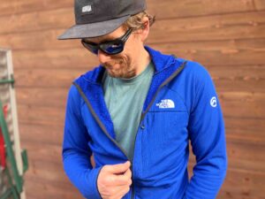 man models The North Face midlayer, in blue, by wooden wall
