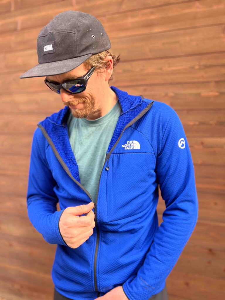 man models The North Face mid layer, in blue, by wooden wall