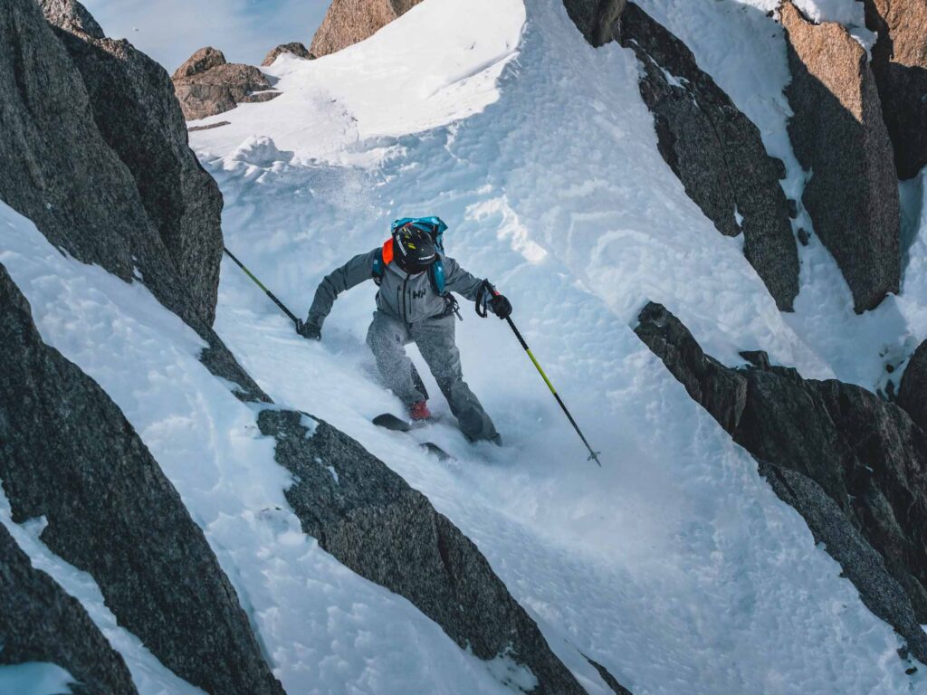 skier, skis sideways, looks down a steep rocky patch of high mountain
