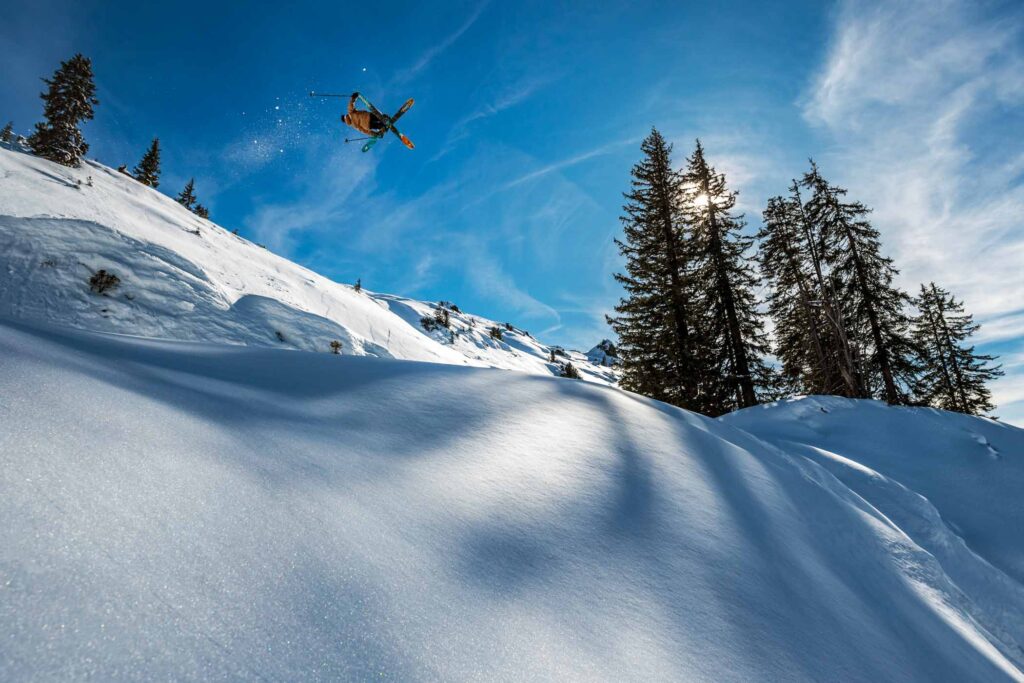 a skier pulls a trick whilst taking big air off piste in pristine snow