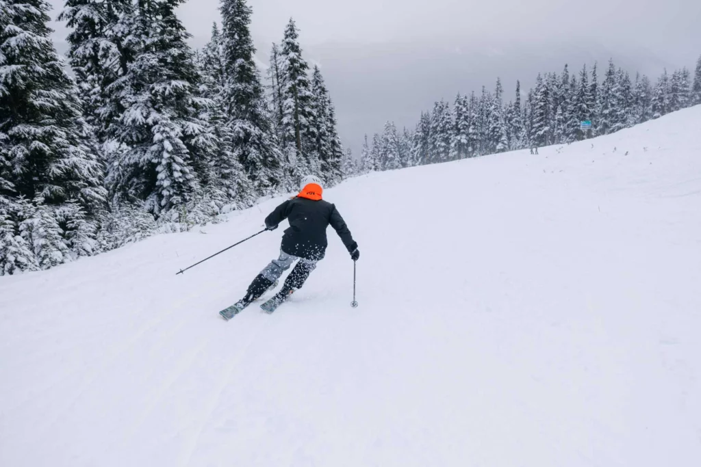 skier in black jacket with orange flash skis on an empty slope as snow comes down