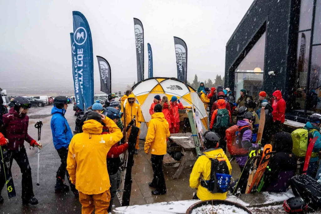 large wet snowflakes come down over group in Gore-Tex jackets by tent outside a ski centre