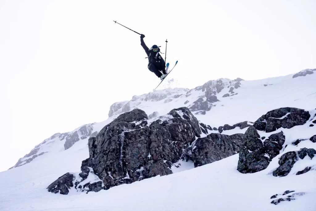 skier takes air, grabbing skis, launching off a big rock