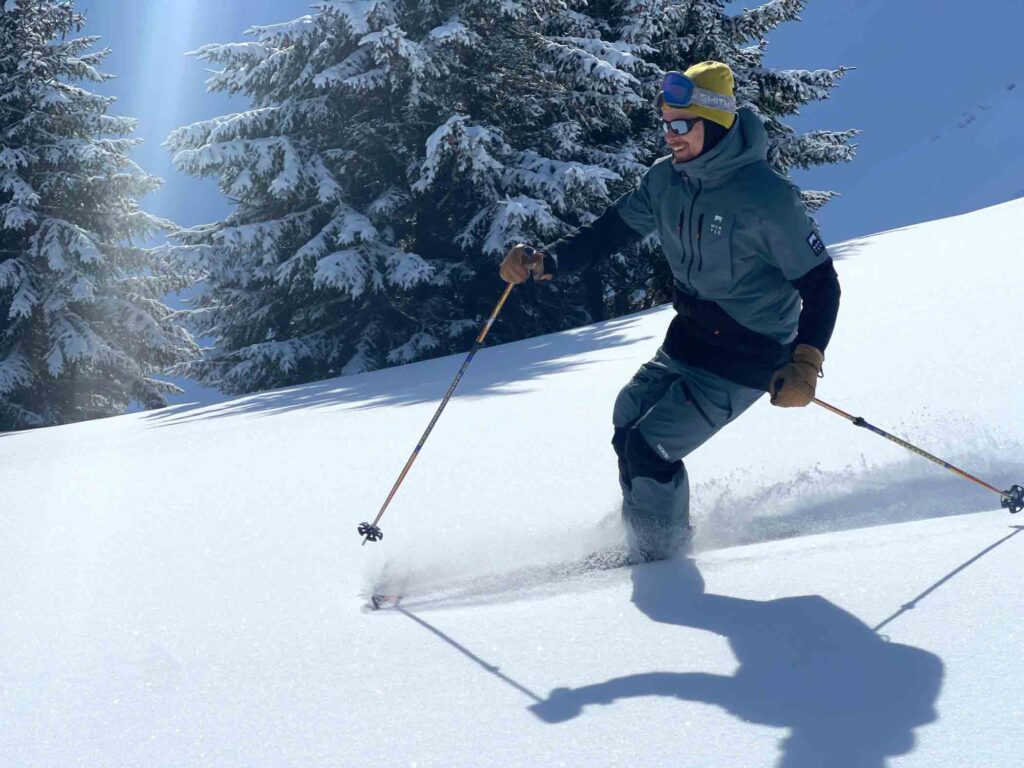 A man skis wearing slate green-black ski gear, skiing on fresh snow on the mountain