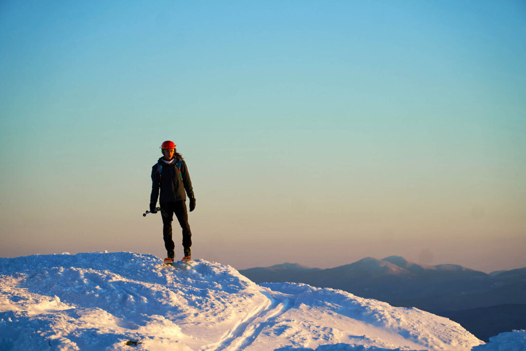 ski touring Noah Dines standing on mountain top on sugary snow, at sunset