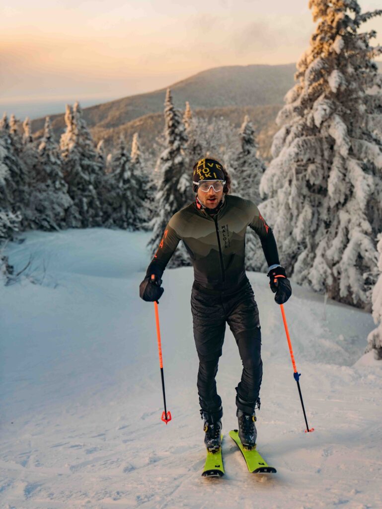 ski tourer uphill through snowy trees in golden light