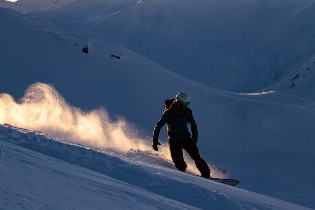snowboarder makes fresh tracks in shade as the sun lights up the dust trail left behind