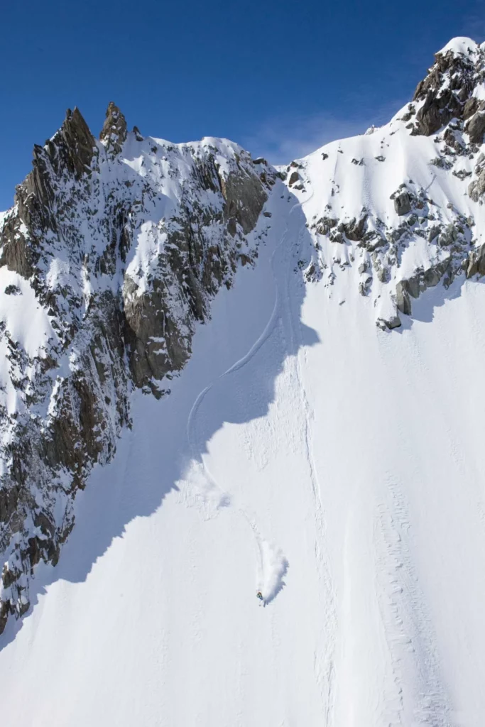 solo skier on a steep open face, below rocks 