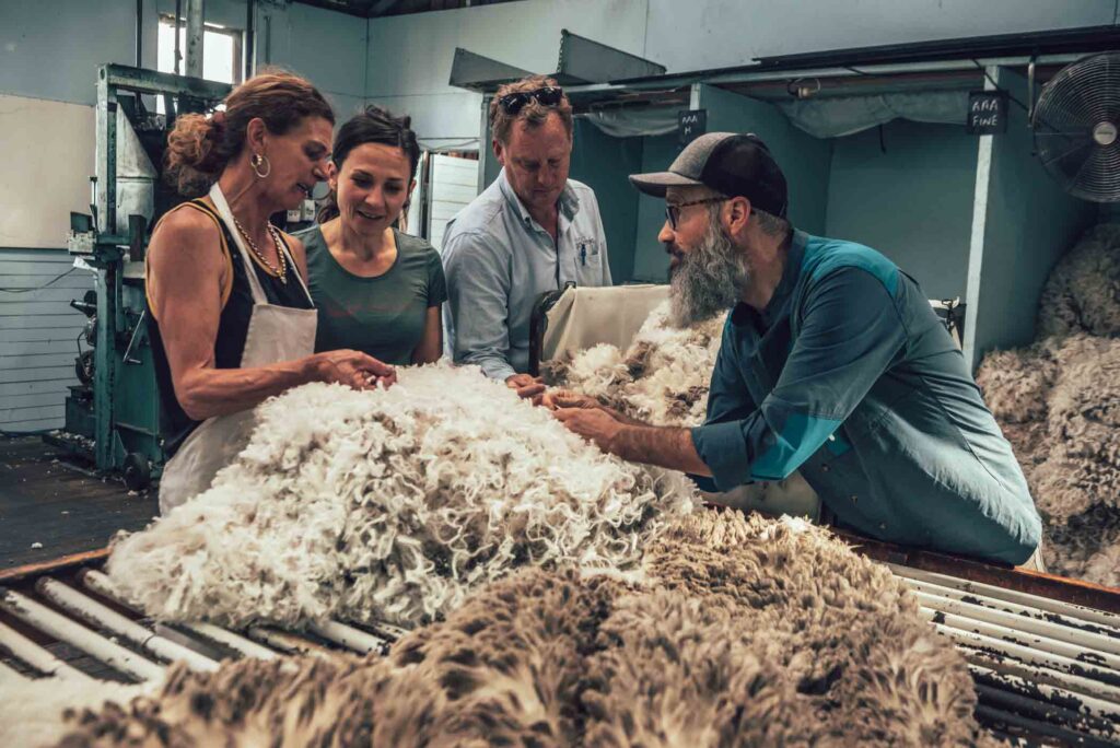 a group of four in a factory holding onto, discussing raw merino wool