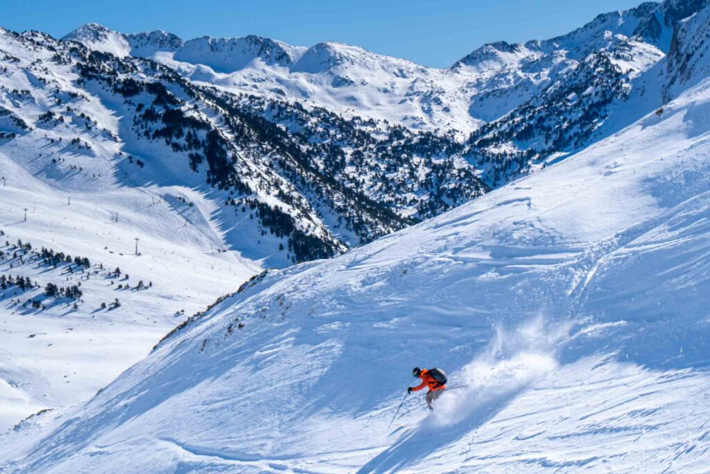 a skier in orange makes fresh tracks off-piste