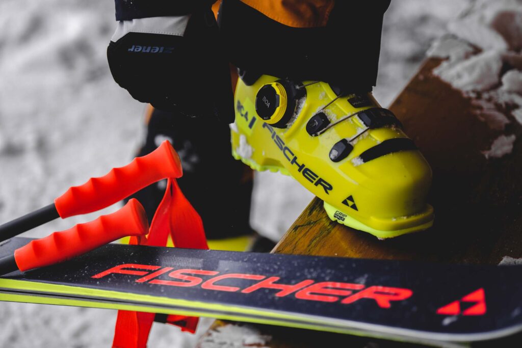 Yellow Fischer RC4 ski boot with BOA fitting placed on wooden bench, with Fischer skis next to it