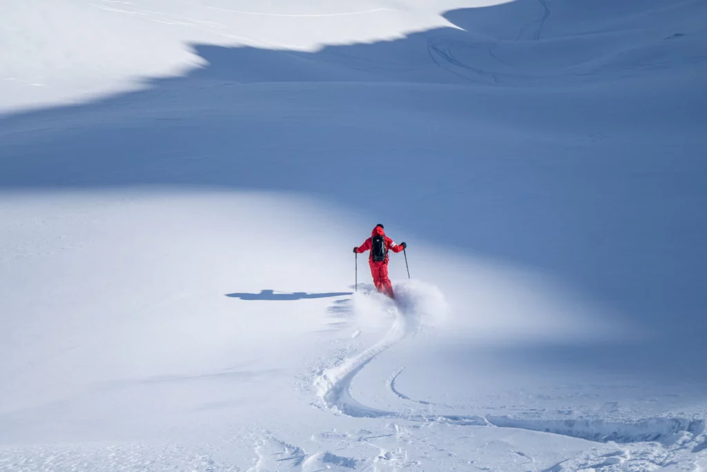 an ESF ski instructor in red makes lovely fresh tracks, arms out to the side, along a shadow line in fresh snow