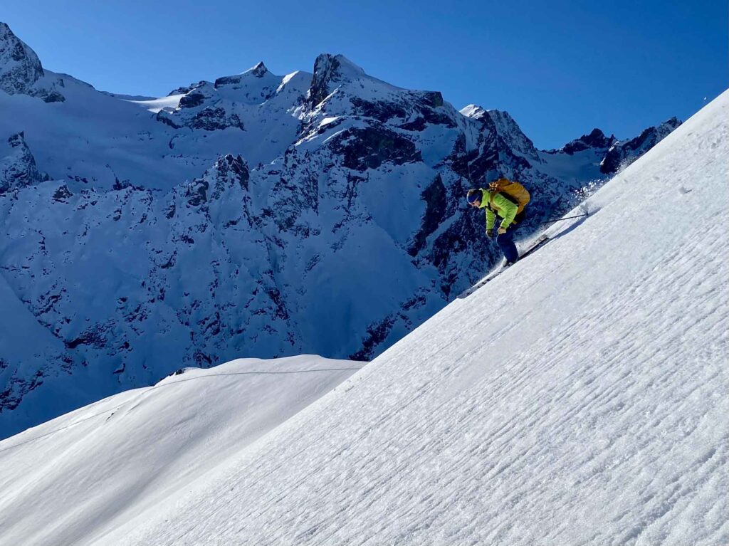 man in bright green jacket and headband on fresh-snow descent, big mountains as a backdrop