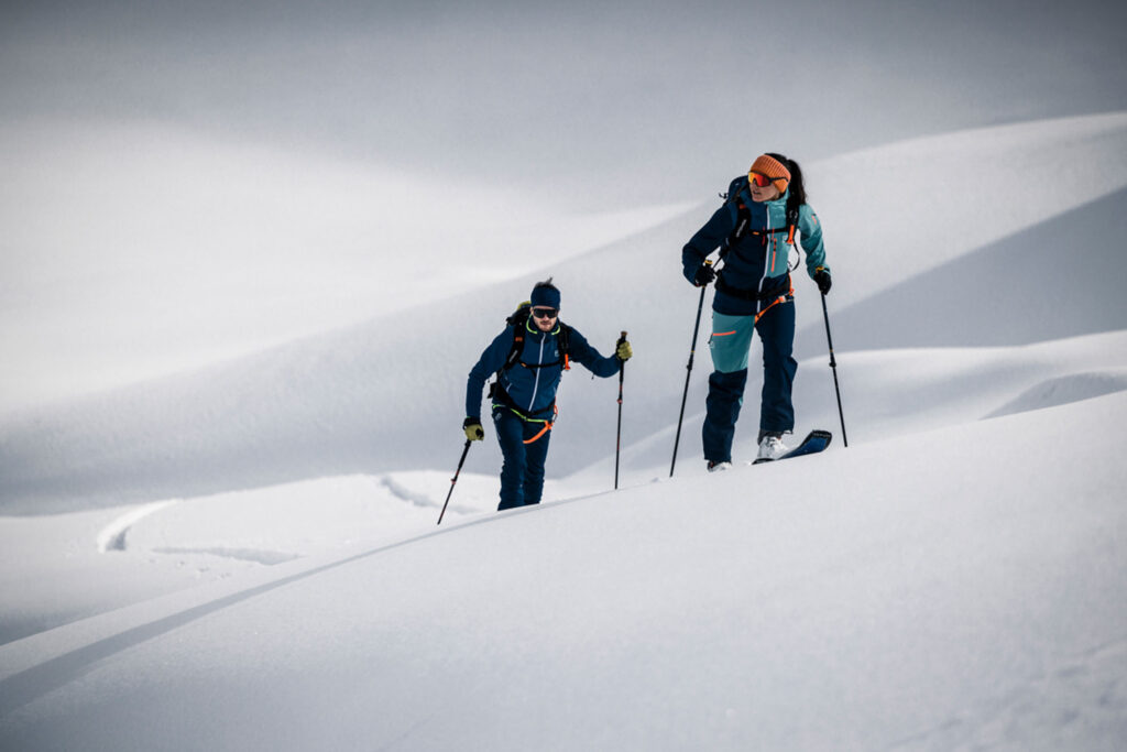 two ski tourers, skinning on fresh undulating snow, no features in the landscape