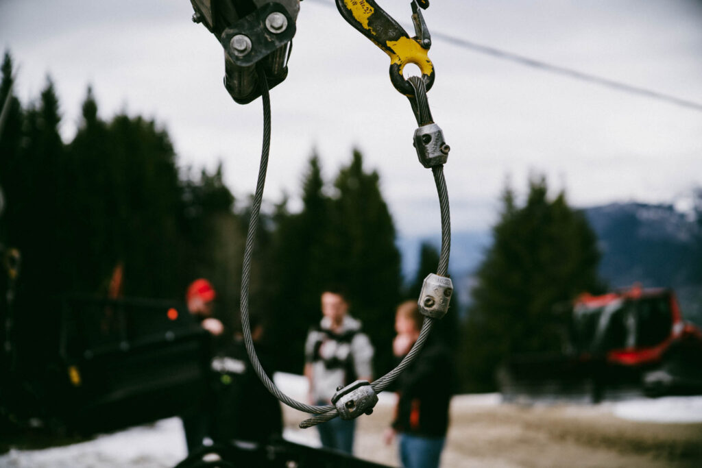 a cable for winching a snow cat to a tree on steep slopes, the background of piste basher drivers blurred