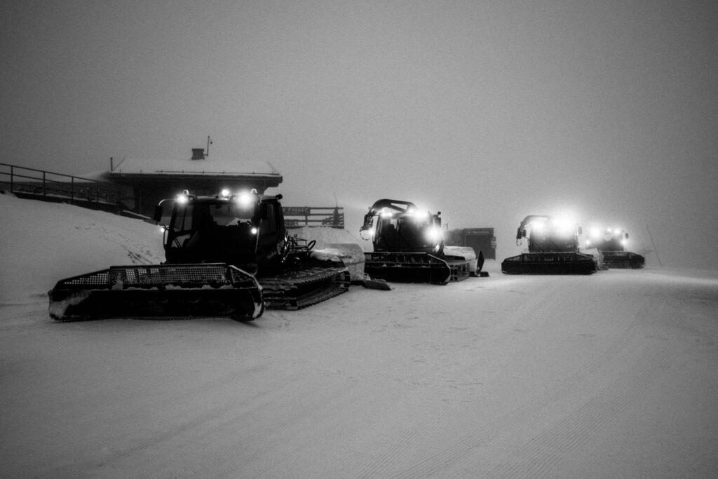 a line of piste bashers, lights on, pictured at night in black and white