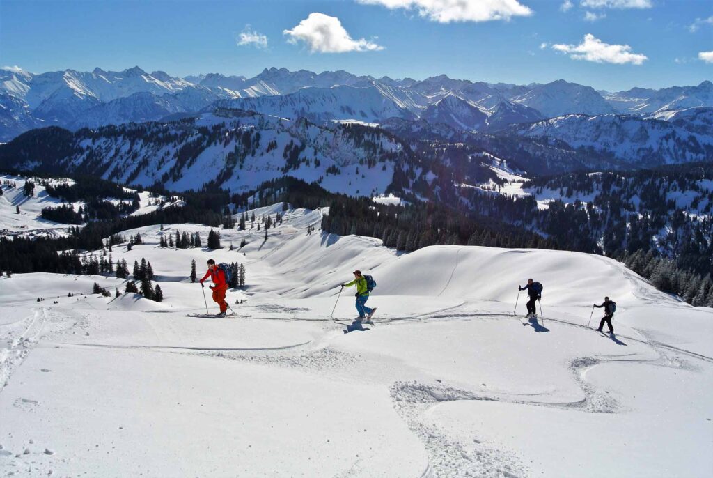 four ski tourers heading uphill under the sun