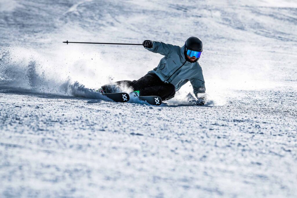 a skier, hip to snow, carve turns deep, pole flung out to the side
