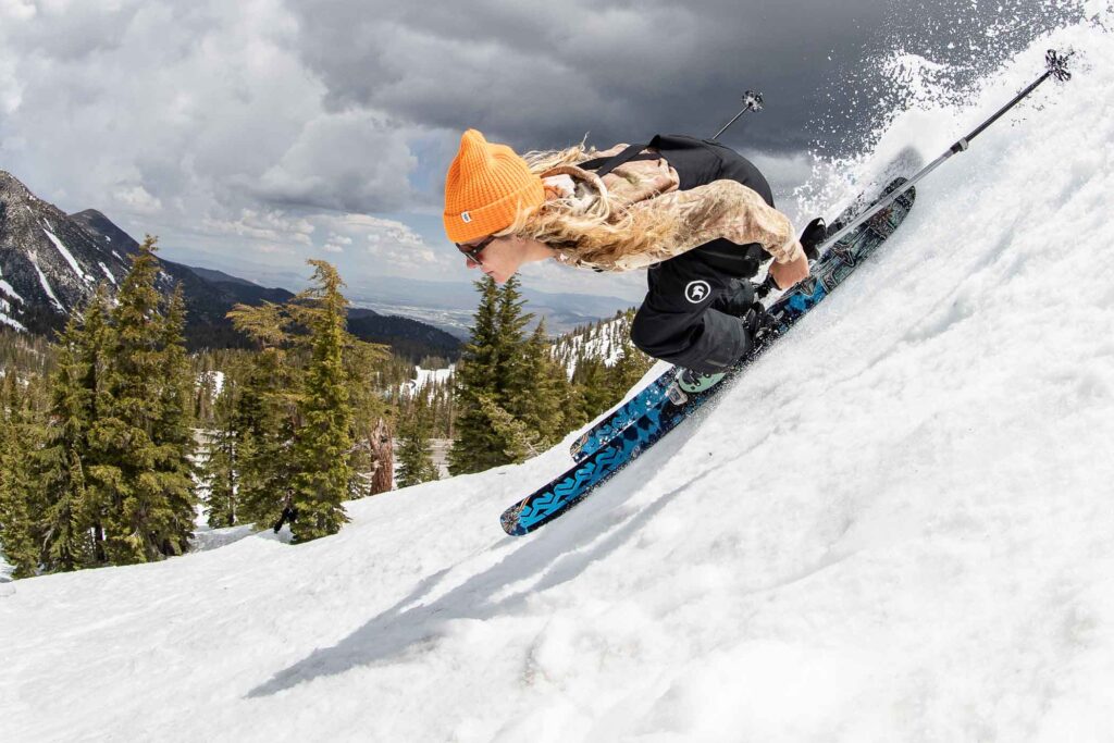 a woman skiing fast downhill, wearing an orange beanie and a t shirt