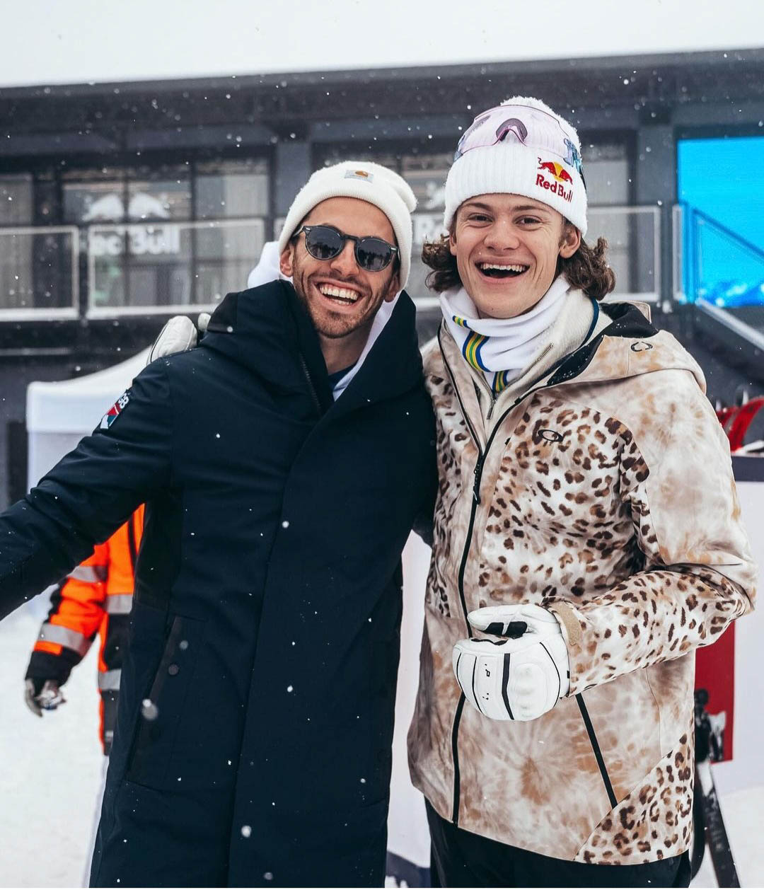 British ski racer Charlie Raposo smiles, arm around ex Norwegian racer Braathen, standing on snow wearing beanies