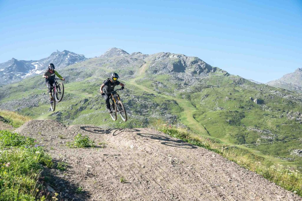 two mountain bike riders take air on a gravel trail, in the high mountains